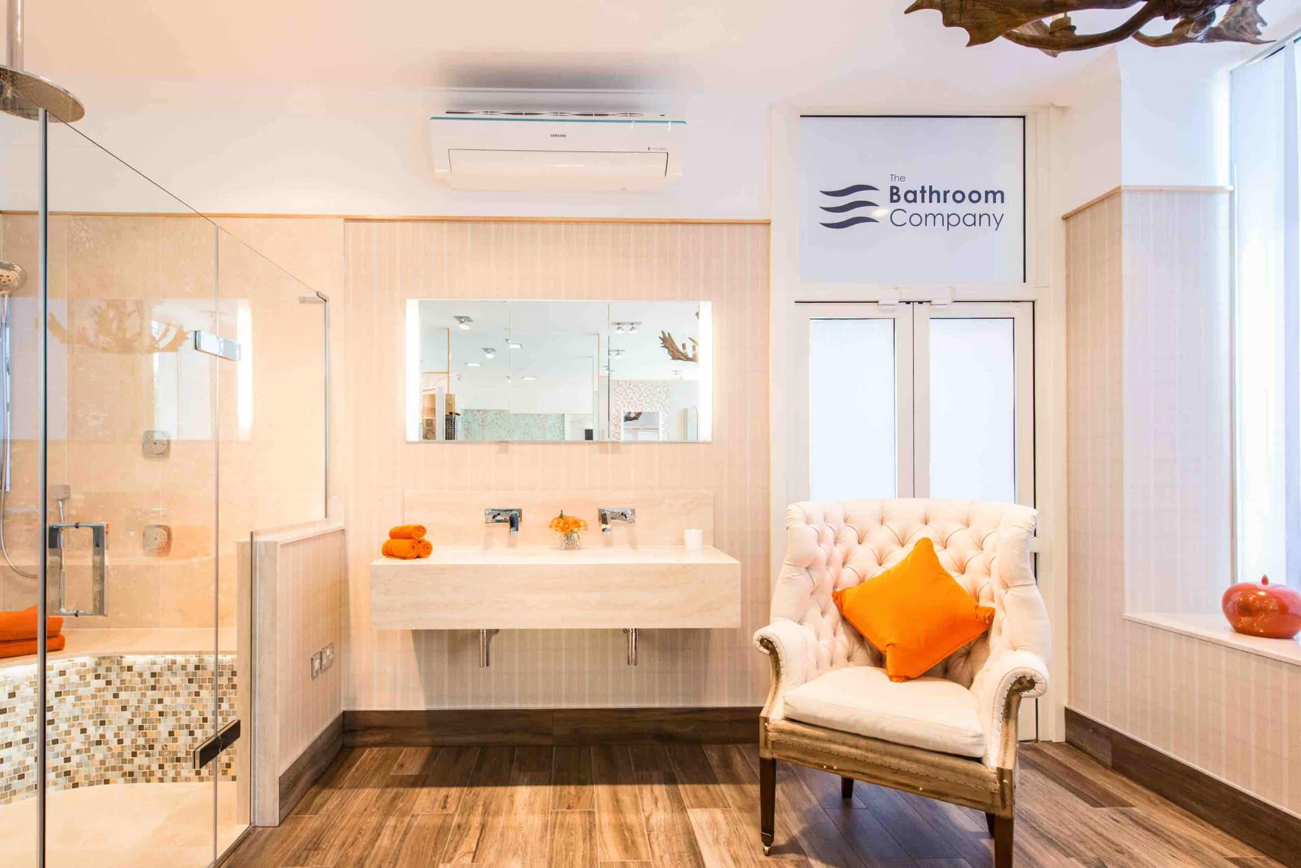 Peach coloured tiles, armchair, large open showering area, wall mounted rectangular mirror and sink
